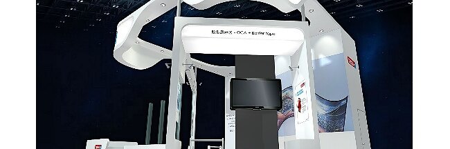 Exhibition booth with a curved, modern design featuring the tesa tape logo prominently displayed. Structures include panels and a screen. The color scheme is primarily white with red and blue accents. The booth is situated in a large, dark exhibit space. (This text has been generated by AI)