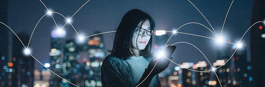 A person wearing glasses looks at a smartphone against a cityscape at night. Bright white lines with glowing nodes crisscross the image, suggesting digital connectivity or communication networks. (This text has been generated by AI)