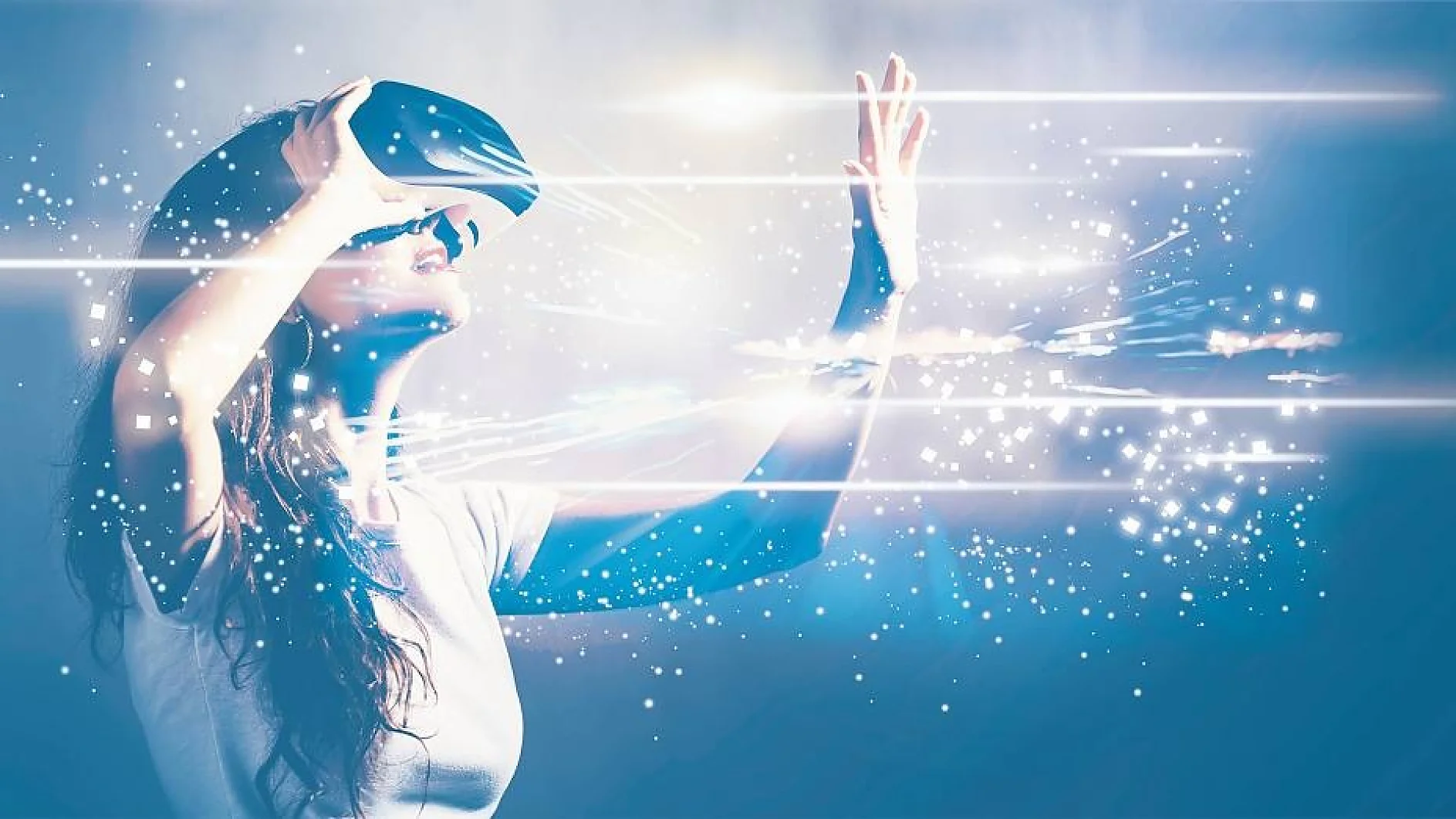 A woman wearing a virtual reality headset reaches out with her hand. Bright, abstract digital light streaks and particles surround her, creating an immersive effect. She is in a white shirt against a blue background. (This text has been generated by AI)