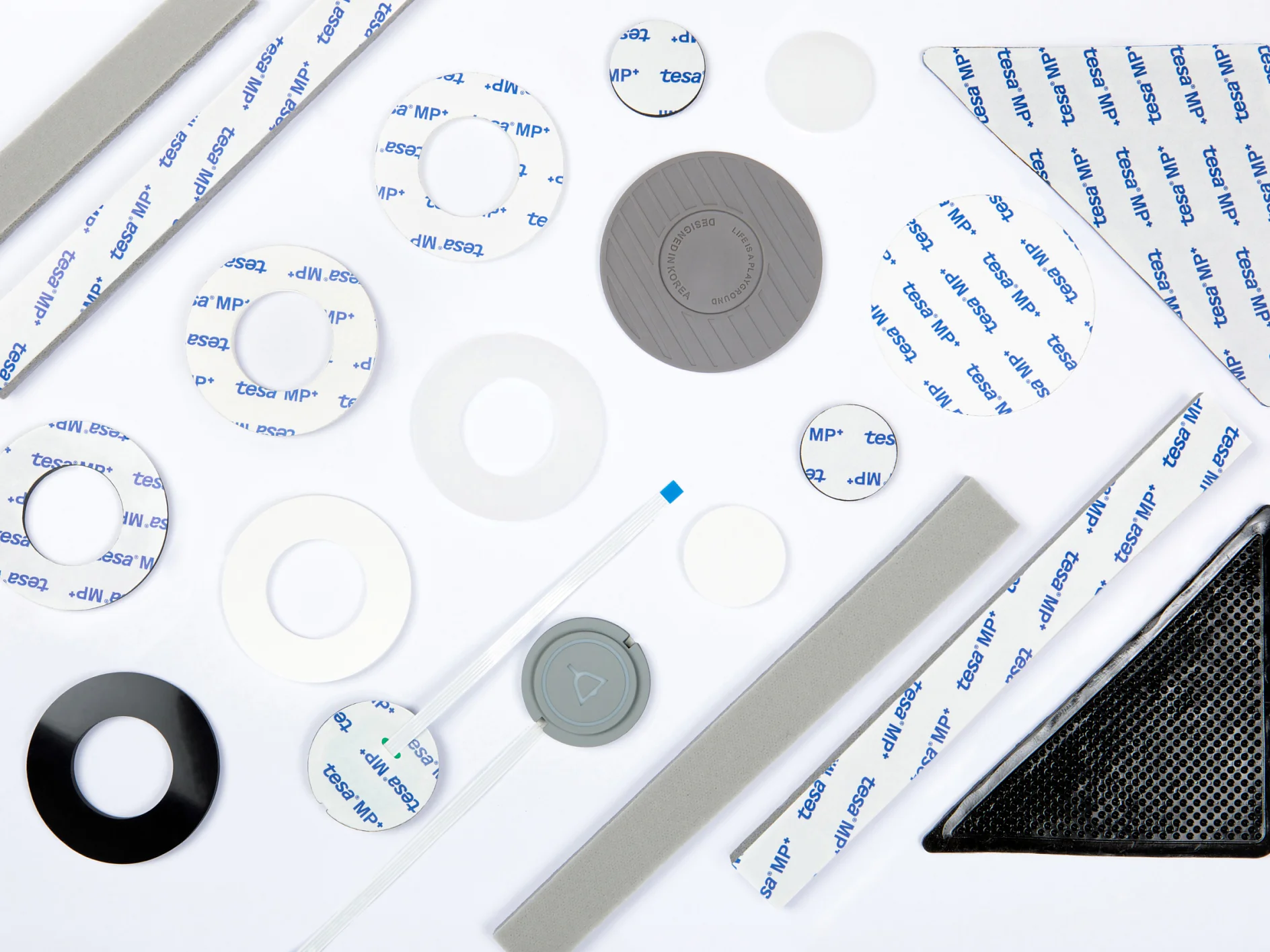 A collection of adhesive foam pads and strips made from tesa tape, available in various shapes and sizes such as circles, rectangles, and triangles, displayed on a white background. Some feature printed text, while others are plain or have a textured surface. (This text has been generated by AI)