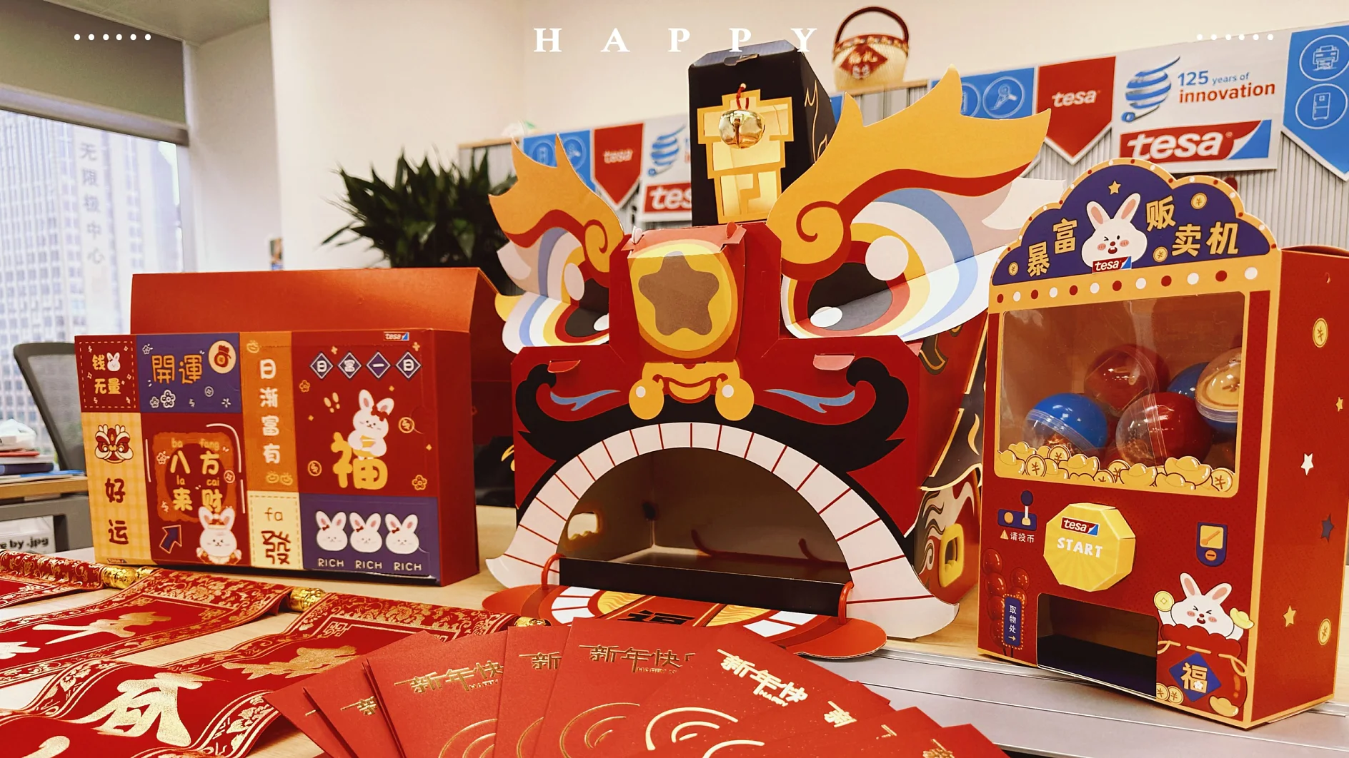 A decorated table with red and gold themed items, featuring a large cardboard dragon head, various red envelopes, a small claw machine, and festive wall hangings. The setting appears to celebrate a festive occasion. (Note: since there were no references to competing brands of tape in your original text, nothing needed changing). (This text has been generated by AI)